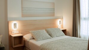 A hotel room with a bed, two bedside tables, a wall-mounted light, and a painting above the bed. - Olea Suites Conil · 3 (Conil de la Frontera)