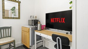 A small room with a desk, a chair, a microwave, a kettle, and a TV displaying 'NETFLIX'. - Park View En-Suite I Egham station (1 miunte walk) (Egham)