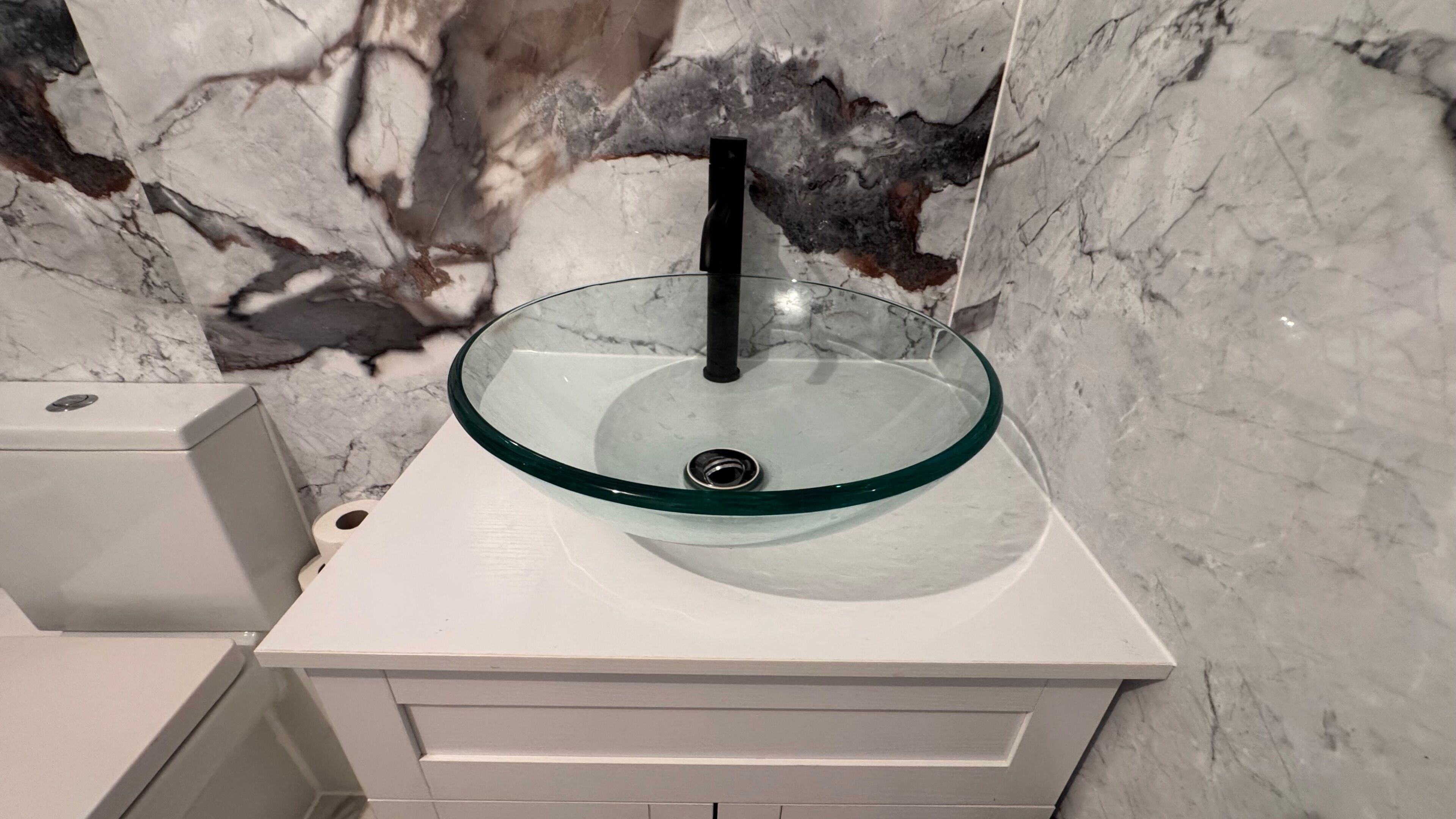 Une salle de bain avec un lavabo en verre, un socle blanc et des murs en marbre.
