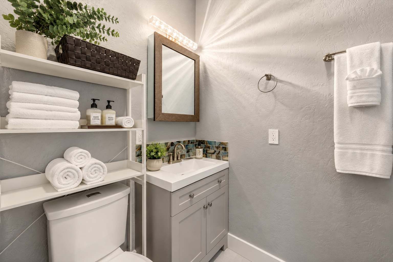 Un bagno con il water, un lavandino, mensole con articoli da toilette, uno specchio e un portasciugamani.