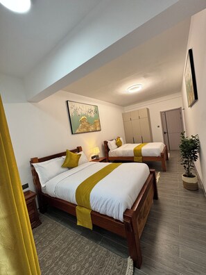 Une chambre d’hôtel avec deux lits en bois, un tableau au mur, une plante en pot et une armoire.