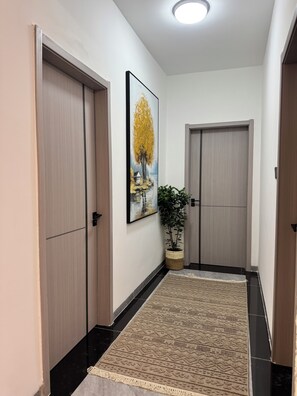 Un couloir avec deux portes, un tableau encadré, une plante en pot et un tapis à motifs.