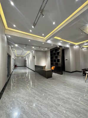 Un hall d’hôtel moderne avec un comptoir d’accueil, un espace salon et une étagère noire.