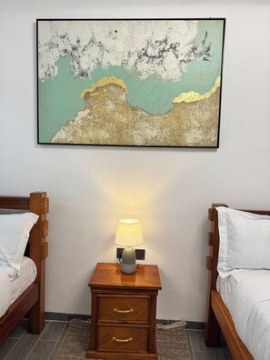 Quarto com duas camas de madeira, uma mesa de cabeceira com abajur e um quadro na parede.