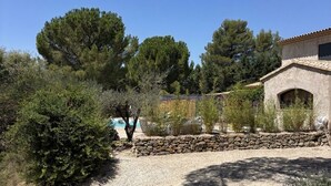 A gravel driveway leading to a house with a stone wall and a pool in the background.