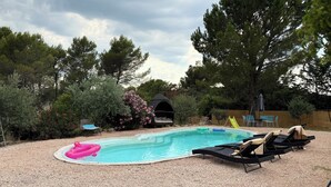 Ein Garten mit Schwimmbecken, Liegestühlen, einem aufblasbaren Planschbecken für Kinder und einer kleinen Gartenanlage mit Bäumen und Sträuchern.