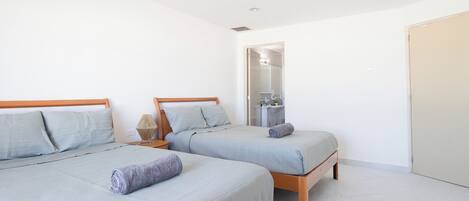 A bedroom with two beds, a bathroom with a mirror, and a door.