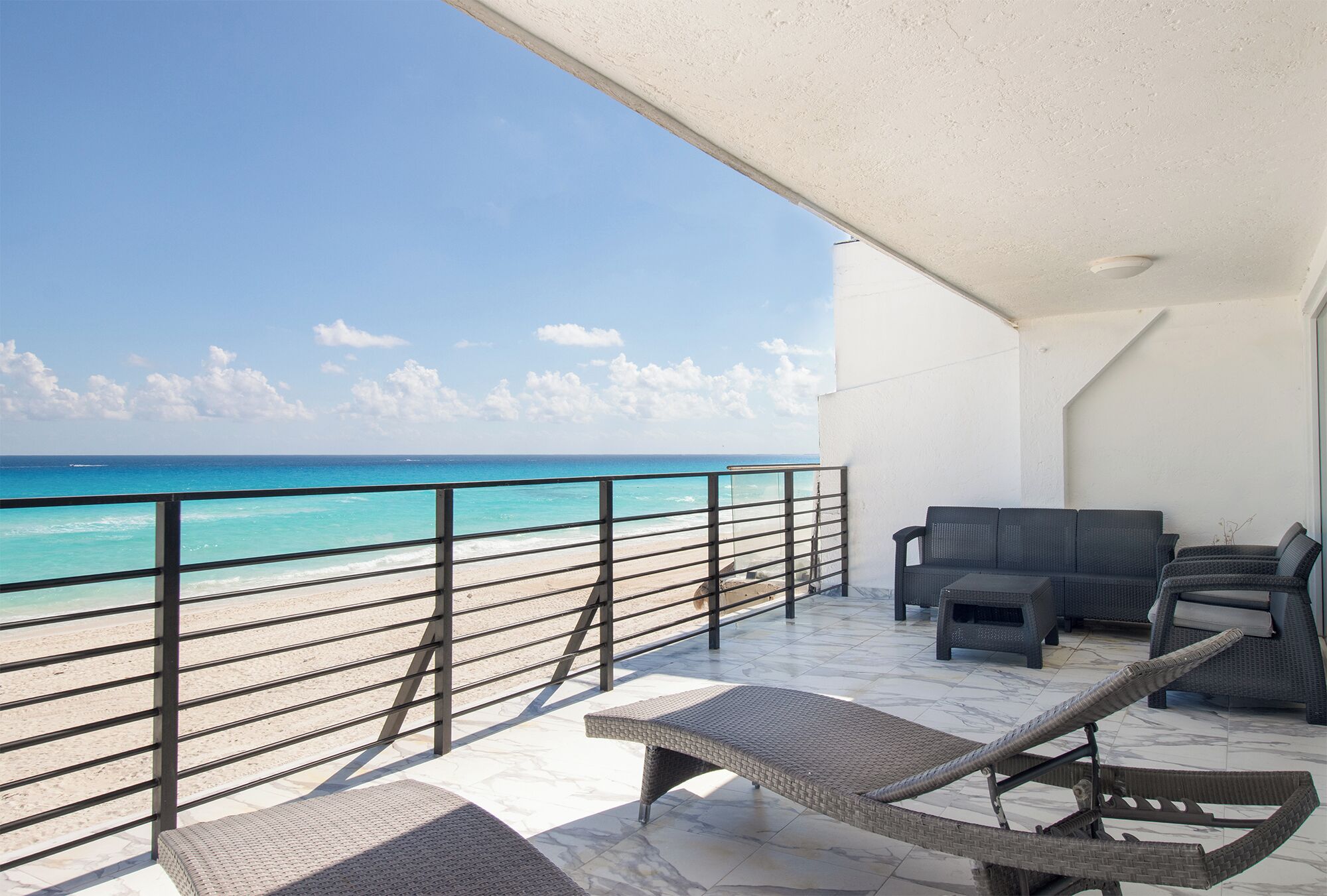 A balcony with a view of the beach, a lounge chair, and a sofa.