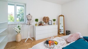 Une chambre à coucher avec un lit, une commode, un miroir, une fenêtre et un vase de fleurs.