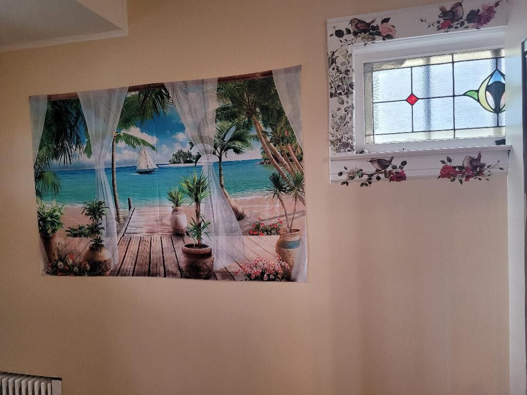 A beach scene with a sailboat, palm trees, and potted plants on a wooden deck.