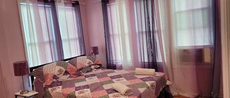 A bedroom with a bed, curtains, a lamp, and a window.