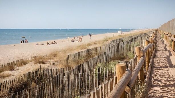 Ein Strand mit einer Holzumzäunung, feinem Sand und dem Meer.