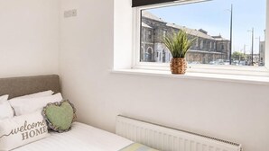 Een slaapkamer met een bed, een raam met uitzicht op gebouwen, een radiator en een stopcontact.