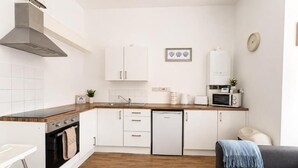 Een kleine keuken met witte kasten, een ingebouwde oven, een vaatwasser en een magnetron.