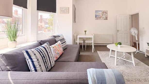 Een woonkamer met een grijze bank, een klein rond tafeltje en een radiator.