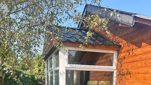 A wooden cabin with a glass door, surrounded by large barrels and potted plants. - Gortin Glen Forest Cabin, Sleeps 7 With Parking (Omagh)
