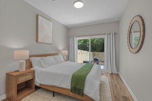 Ein Schlafzimmer mit einem Bett, Nachttischen, einem Spiegel und Blick ins Freie.