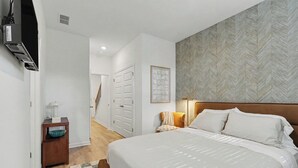 A bedroom with a large bed, a nightstand, a wall-mounted TV, and a patterned wall. - Grant & Groove: Where timeless design meets the rhythm of ATL. (Atlanta)