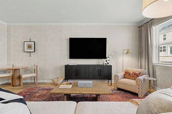 Una sala de estar moderna con una televisión de pantalla plana, una mesa de centro de madera, un sofá y una alfombra estampada.