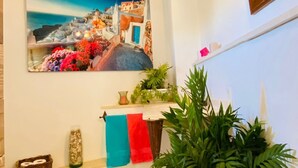 A bathroom with a stone floor, a large potted plant, a painting of a coastal scene, and a wooden ceiling beam. - Country House in Gaucin (Gaucín)