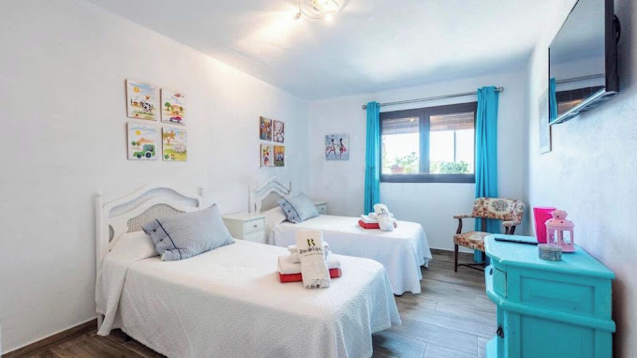 A bedroom with two beds, a window with curtains, a TV, and artwork on the walls.