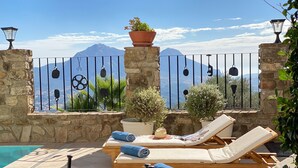 A poolside area with lounge chairs, a stone wall, and a view of mountains. - Country House in Gaucin (Gaucín)
