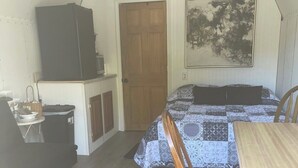Una habitación pequeña con cama, mesa, silla, armario y puerta.