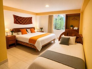 A hotel room with two beds, a large window, a wooden headboard, a bedside table with a lamp, and a wall-mounted tapestry. - Luz y Amistad - Pisac (Pisac)