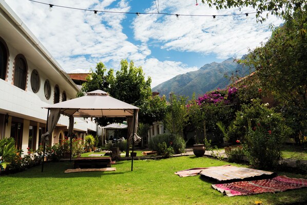 Un patio con pérgola, mobiliario exterior y montañas al fondo.
