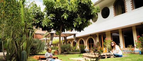Un patio exterior con un árbol, una banca y un edificio con ventanas de arco.