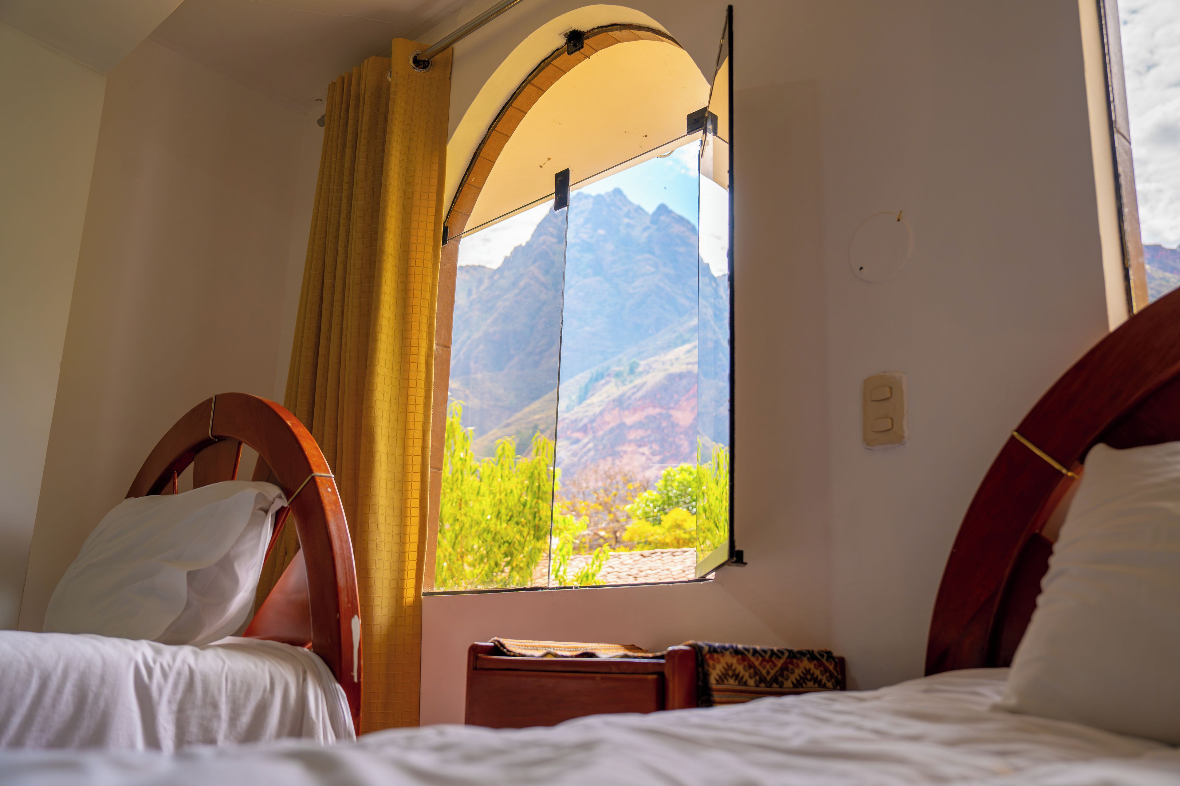 Una habitación con dos camas, una ventana con vista a las montañas y una cortina.