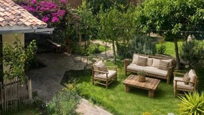 Un patio con un sendero de piedra, muebles de madera y plantas en macetas.