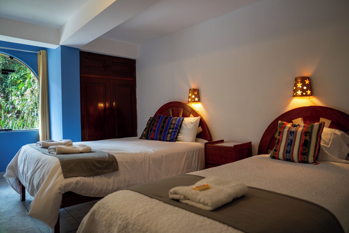A hotel room with two beds, a window with curtains, and a door.