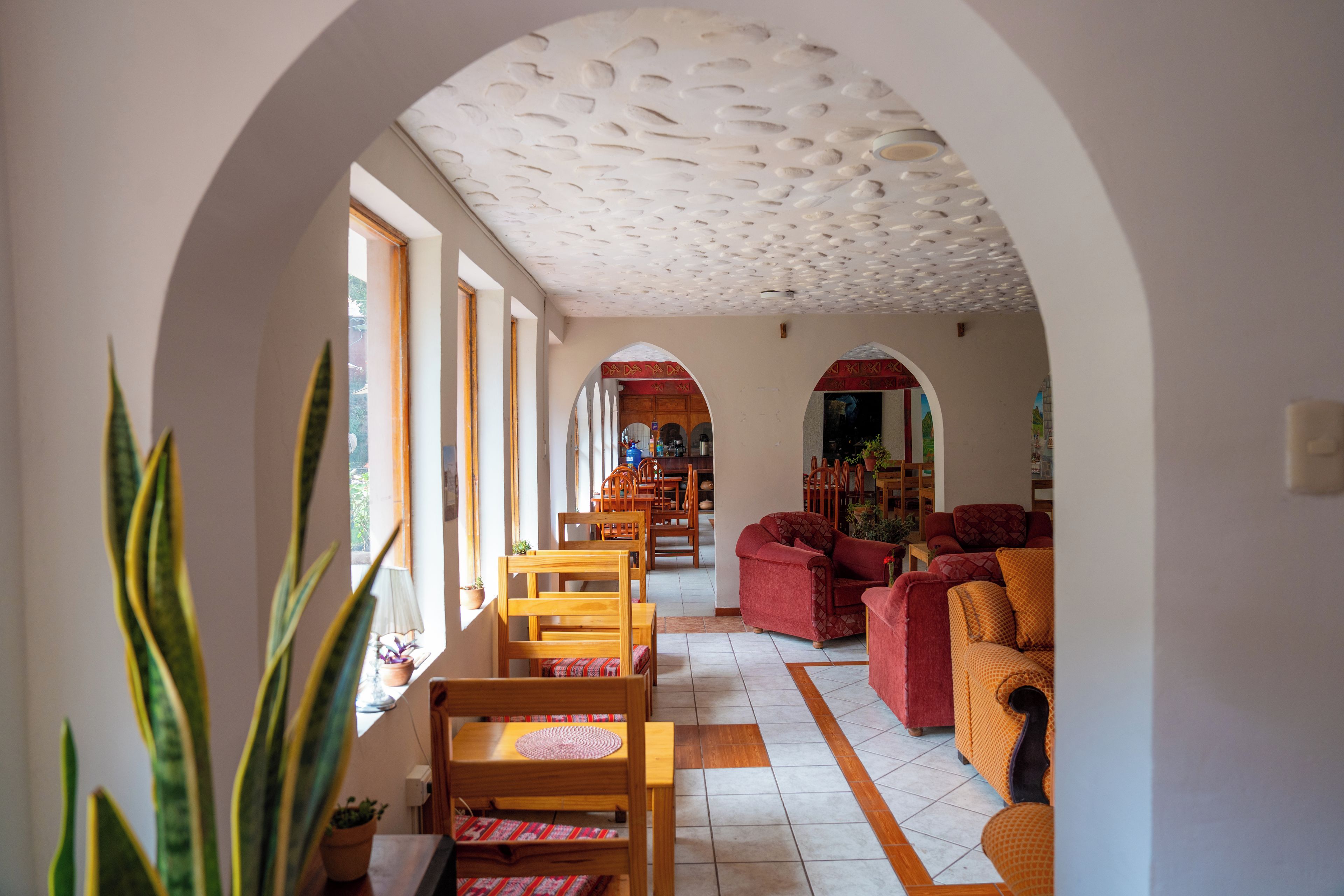 A spacious living area with a high ceiling, wooden furniture, and a view through an arched doorway.