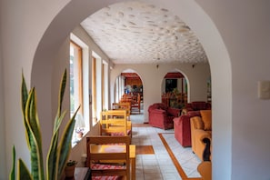 A spacious living area with a high ceiling, wooden furniture, and a view through an arched doorway. - Luz y Amistad - Pisac (Pisac)