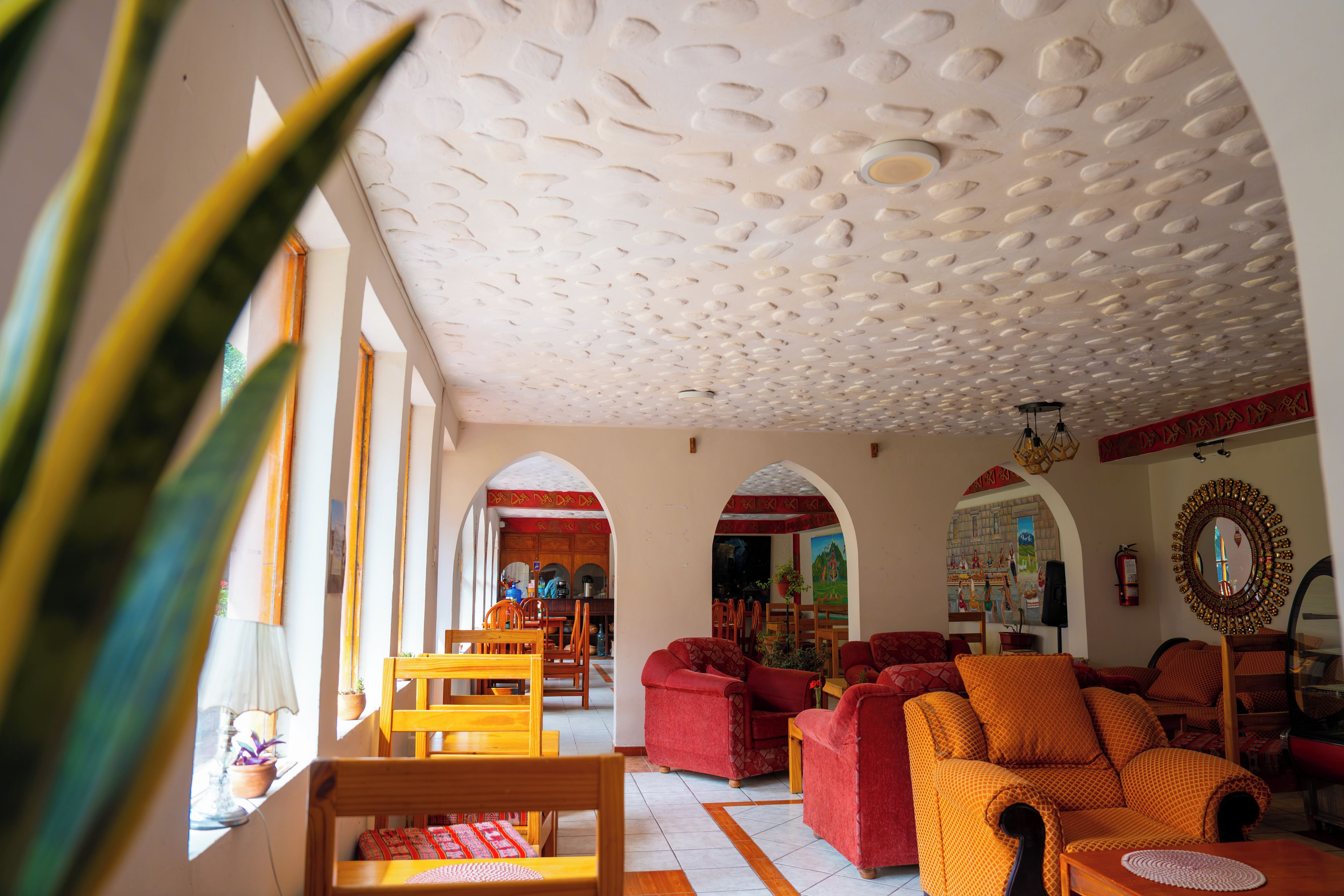 A spacious living area with a high ceiling, wooden furniture, and a view through an archway to a kitchen area.