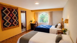 Habitación de hotel con dos camas, un ventanal grande, un tapiz en la pared y una mesita de noche con una lámpara.