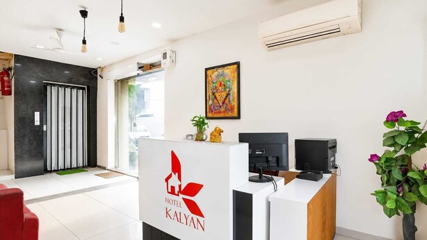 A hotel reception desk with a logo, a fire extinguisher, a plant, and a painting on the wall. - HOTEL KALYAN (Rajkot)
