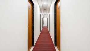 A hotel hallway with a red carpet, wooden doors, and a white wall. - HOTEL KALYAN (Rajkot)