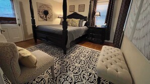 A bedroom with a four-poster bed, a ceiling fan, a patterned rug, a nightstand, and a chair. - Walk to Main Street, Hot tub, Fireplace! (Fredericksburg)