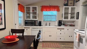A compact kitchen with white cabinets, a microwave, a coffee maker, and a dining table with a red bowl. - Walk to Main Street, Hot tub, Fireplace! (Fredericksburg)