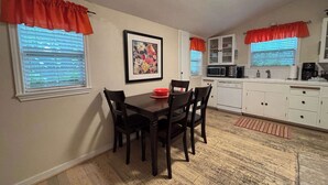 A compact kitchen with white cabinets, a dining table with chairs, and a microwave. - Walk to Main Street, Hot tub, Fireplace! (Fredericksburg)
