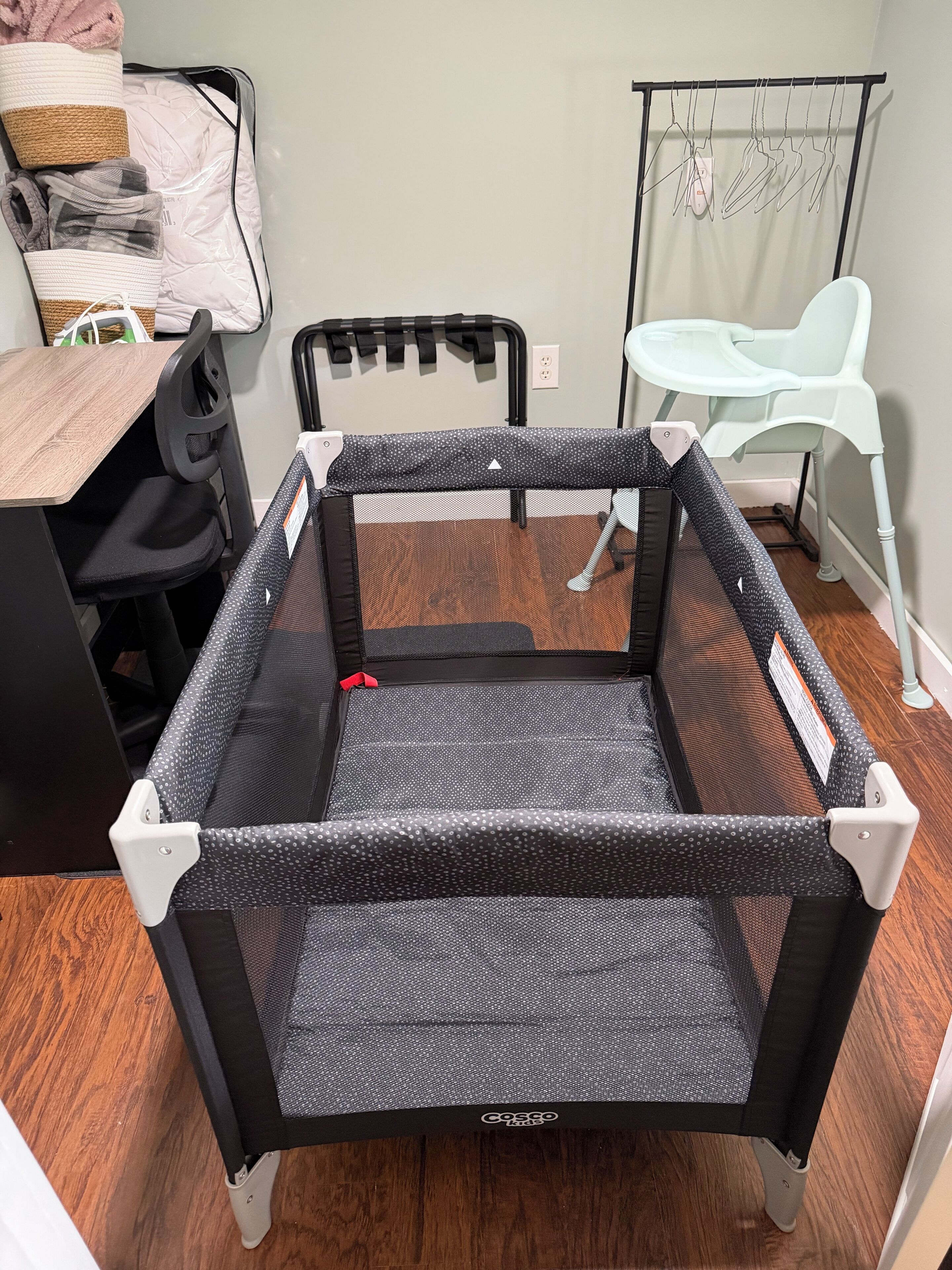 A room with a cot, a chair, a table, and a hanging clothes rack.