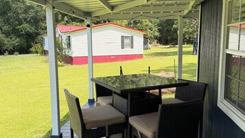 A covered patio with a table and chairs, a view of a house in the background, and a grassy yard.