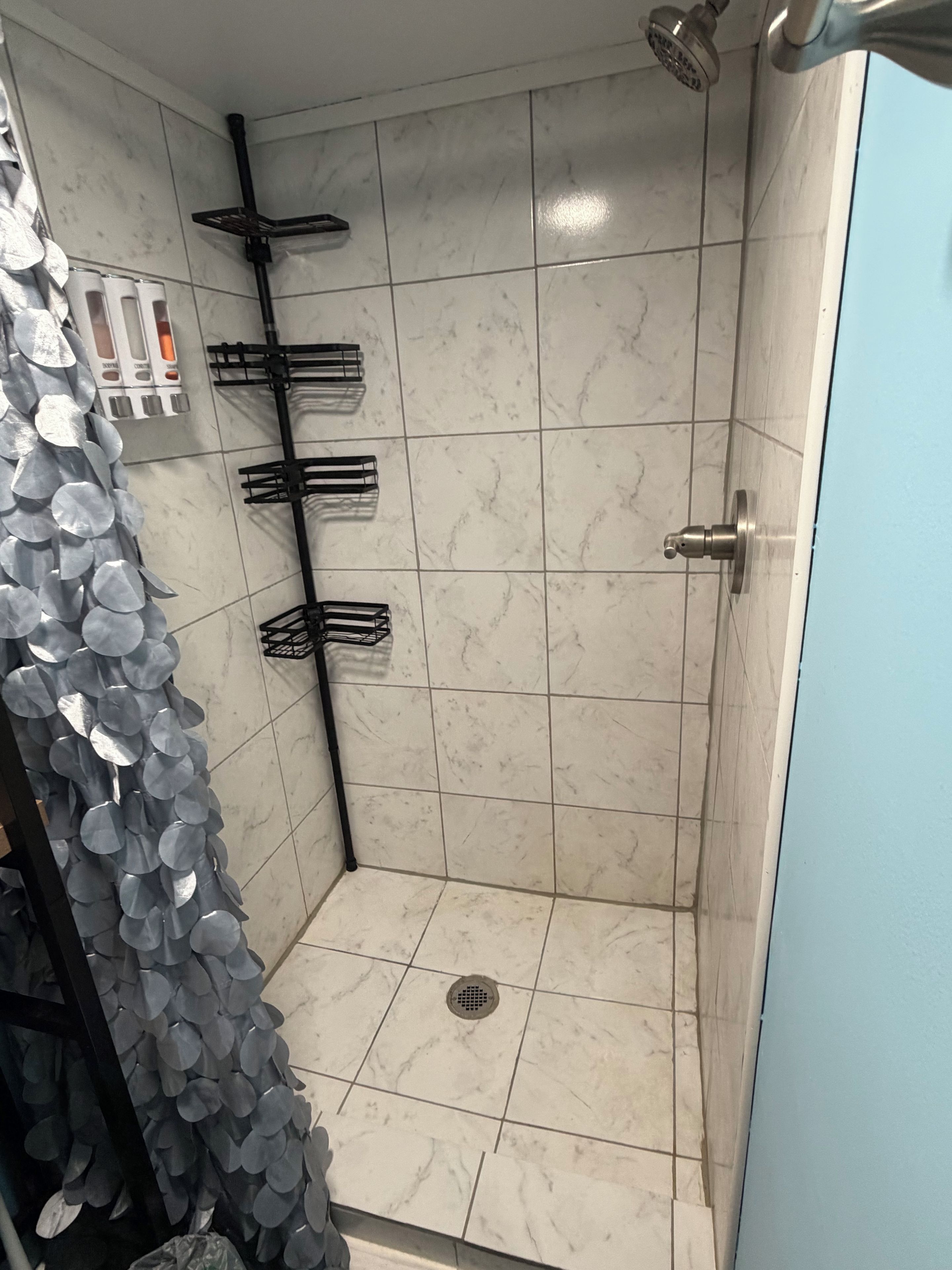 Eine Dusche mit Abfluss, einem Metallregal und einem am Wand montierten Wasserhahn.