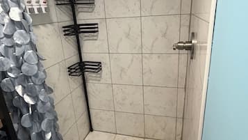 Eine Dusche mit Abfluss, einem Metallregal und einem am Wand montierten Wasserhahn.