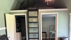 Une pièce avec un canapé en cuir noir, un plancher en bois, un ventilateur de plafond et une échelle menant à une mezzanine.