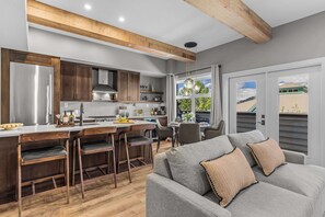 Een moderne keuken met houten kastjes, een bar en een eethoek met een grijze bank en decoratieve kussens.