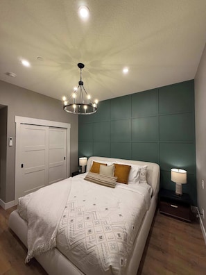 A bedroom with a bed, a chandelier, a nightstand, and a door. - BRAND NEW Luxury Downtown Condo Settlers on Main (Canmore)