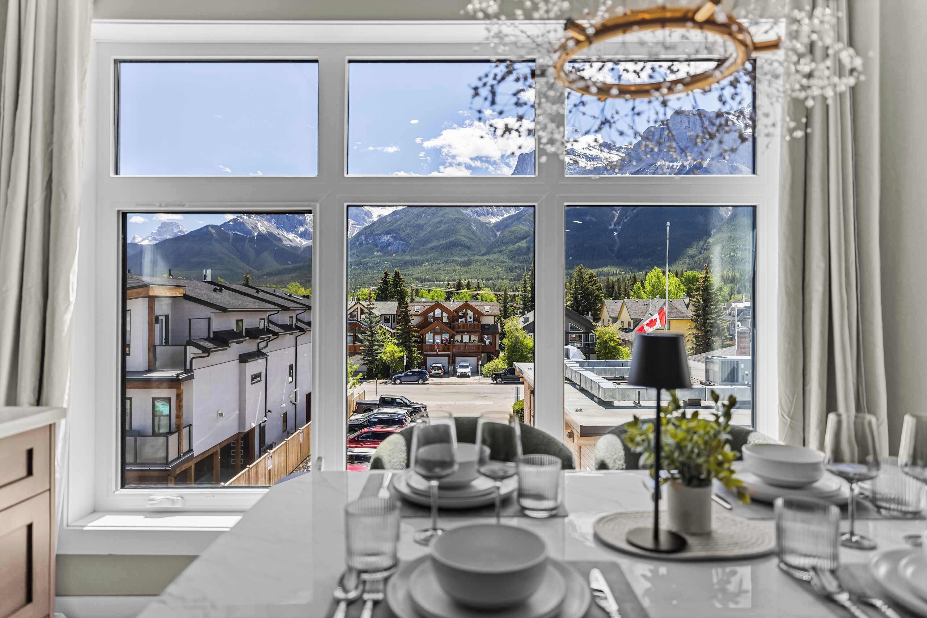 Un coin repas avec une table dressée pour six personnes, une vue sur un paysage montagneux par une grande fenêtre et un lustre.